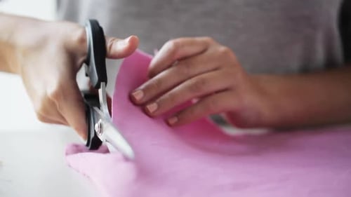 Woman Cutting Pink Fabric with Scissors on Table