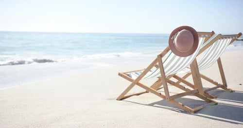 A deck chair and hat on a beach depict a serene, sunny day.