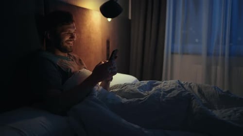 Apartment Bedroom Handsome Young Man Using Smartphone in Bed at Night
