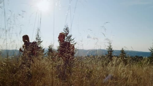Two Men Hiking with Backpacks Through Mountain Grass