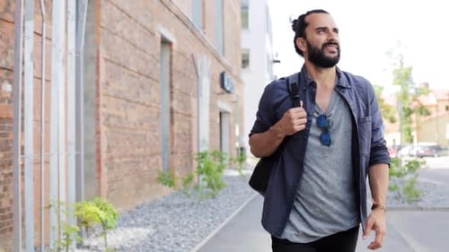 Bearded man walks confidently along city sidewalk
