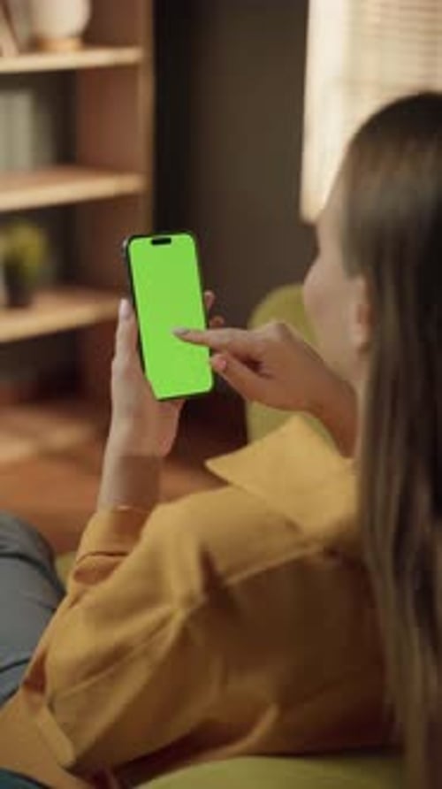 Woman Holding a Modern Smartphone with a Vivid Green Screen Actively Tapping on the Display While