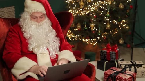 Santa Claus Working on Laptop by Christmas Tree