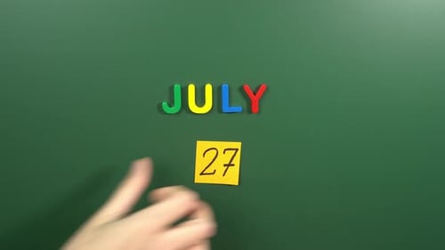 Hand sticking a sticker 27 July calendar day on school board. 27 date of July. Twenty seventh day