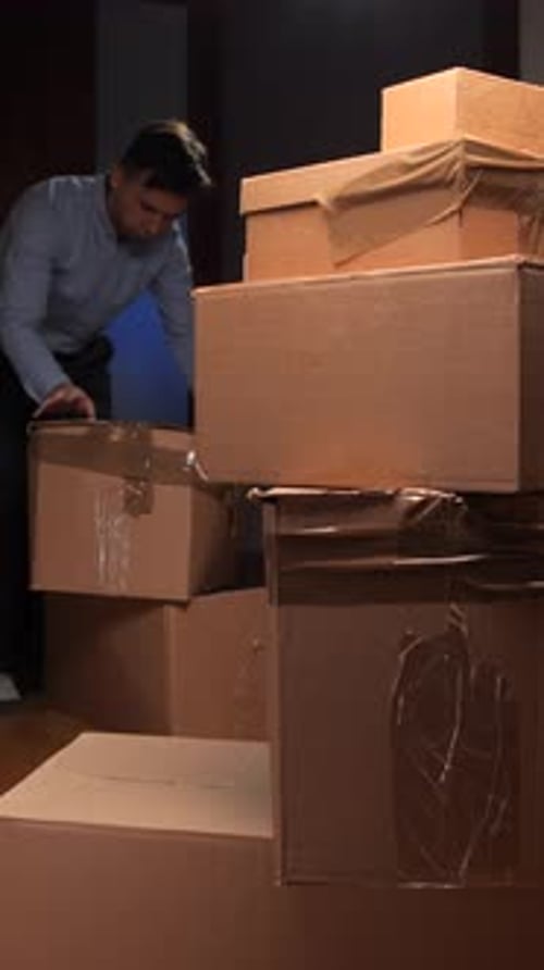 Man Stacking Cardboard Boxes in a Dark Room