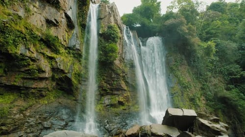 Powerful Nauyaca waterfall flowing over mossy cliffs into green jungle basin