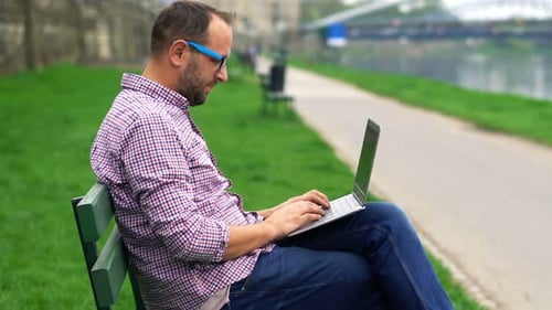Young Man Sitting with Laptop on Bench in the Park 30s