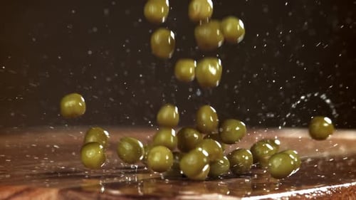Green Peas Falling onto Glossy Wood Surface