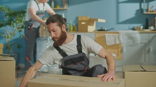 Worker of Moving Company Using Duct Tape Machine for Packing a Cardboard Box