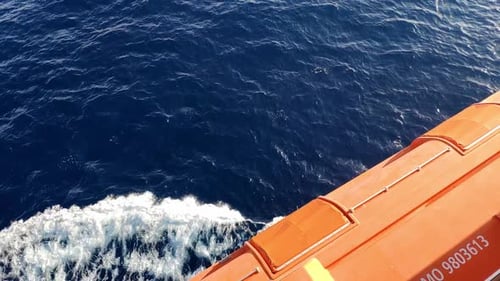 View of the sea while navigating on a cruiser. Orange life boat above sea water on camera. Sailing i