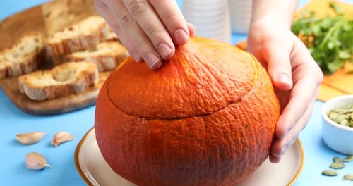 Woman with tasty pumpkin cream soup with seeds and parsley served in pumpkin at blue wooden table