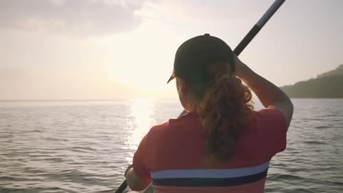 Woman paddle on an inflatable kayak with dog in cap holds on the calm surface of sea