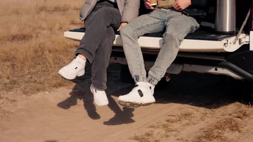 A guy and a girl are sitting together in the open trunk of a crossover talking and squinting the sun