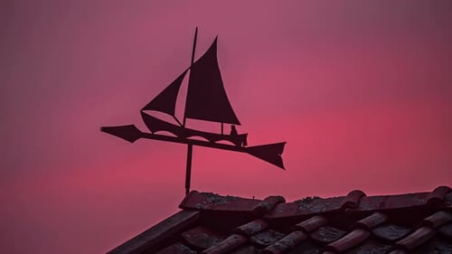 Niedrigwinkelaufnahme einer künstlerischen Wind- oder Wetterfahne, die sich an einem bewölkten Abend auf dem R im Zeitraffer bewegt