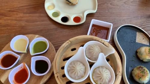 Chinese Dimsum neatly plated on a wooden table with a colorful array of dipping sauces. Hand using c