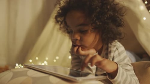 Petit enfant choisissant une vidéo sur tablette dans une chambre onirique la nuit