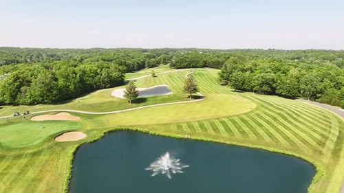 Drone view of a green golf course with grass cut lines and beautiful trees.