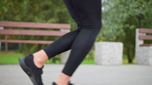 Sporty Woman Jogging in Black Leggings and Sneakers in Park with Trees and Bench