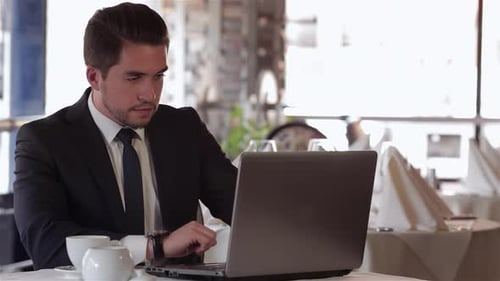 Focused Man Working on Laptop During a Business Lunch at a Stylish Cafe