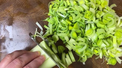 Knife Chopping Leeks on Wooden Cutting Board