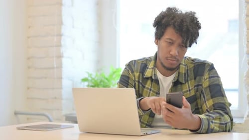 African Man Browsing Smartphone while Sitting in Office