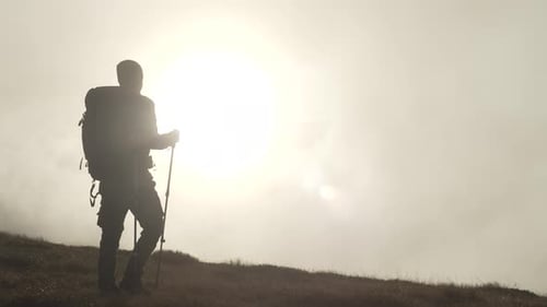 A Hiker with a Backpack Climbs a Mountain at Sunset