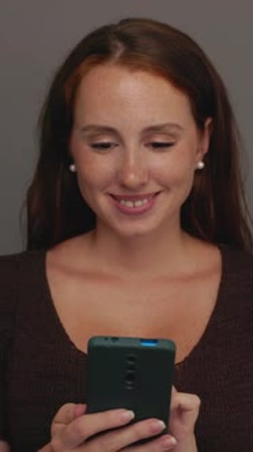 Young Happy Ginger Woman Using Smart Phone Device Over Studio Background