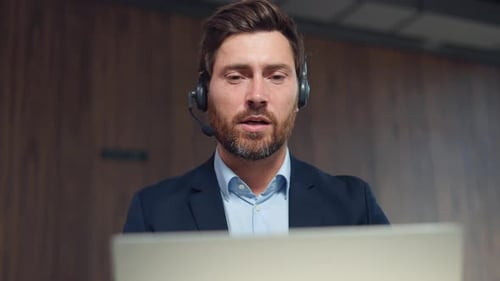 Focused Man in Suit Using Headset and Computer
