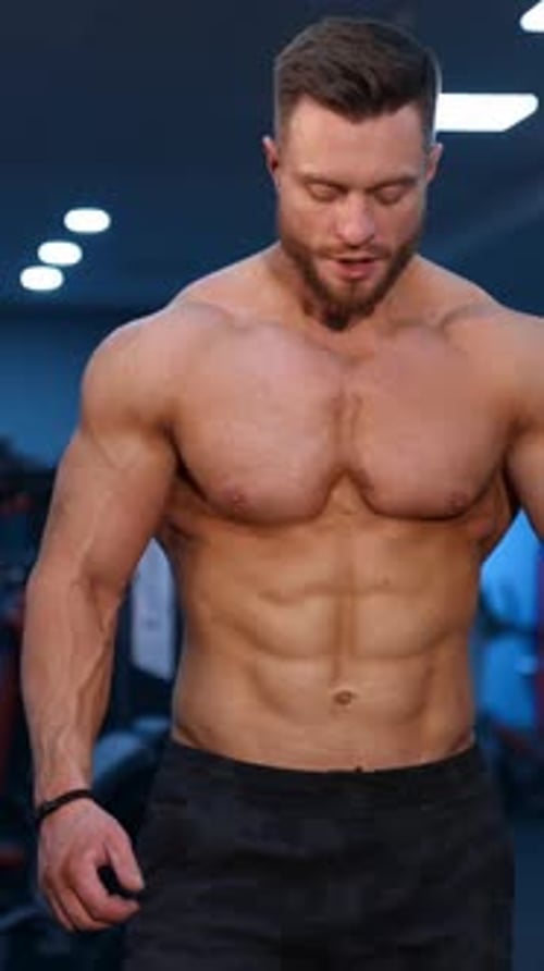 Muscle athlete strongman walks in a gym after heavy training. Perfect torso with strong abs.