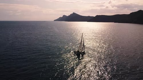 Sailboat sailing by coastline seashore against sunset and mountains. Sail boat in the south coast