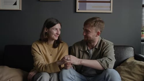 Smiling Couple Holding Hands on Sofa at Home