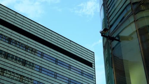 Moderne Gebäude, die sich schräg schneiden, mit einer Sicherheitskamera im Vordergrund vor blauem Himmel