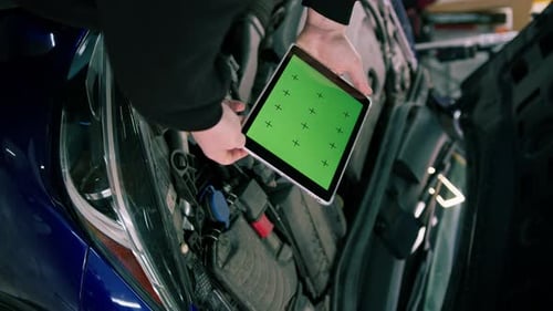 Male car service worker with a tablet in his hands on which there is a green screen near the hood
