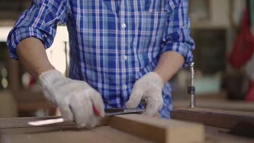 Asian senior carpenter using ruler to measuring wood board at the carpentry workshop.