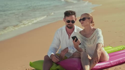 Young Restful Couple in Sunglasses Relaxing on Mattresses on Sandy Beach