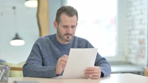 Middle Aged Man Reading Documents in Office, Paperwork