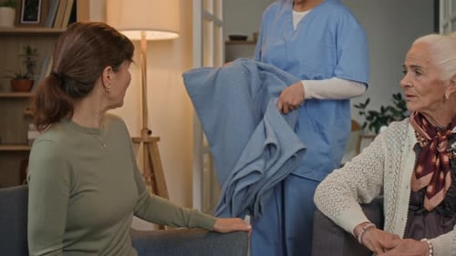 Woman receiving blanket from caregiver while conversing with friend