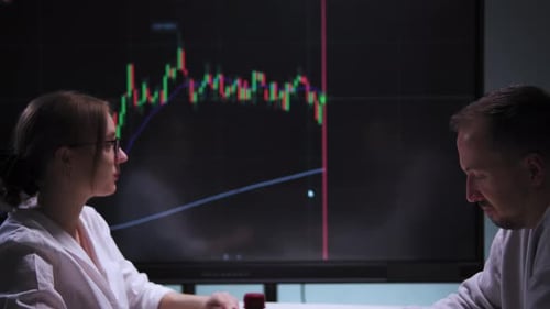 Discussion Among Employees at a Table in an Office with a Stock Market Chart