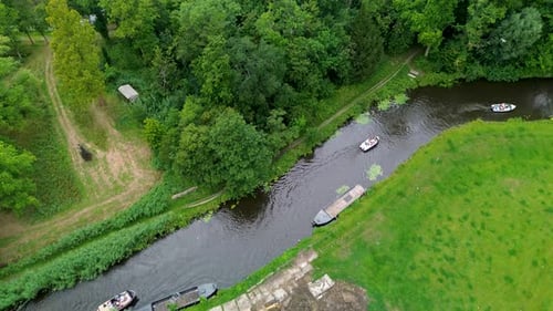 Aerial view of a narrow river with boats cruising along the banks, lush green trees, grassy fields