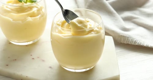 Woman eating delicious vanilla pudding at white wooden table, closeup