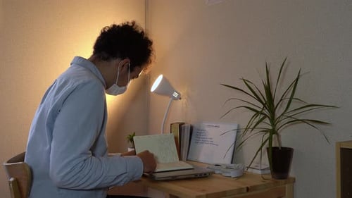 Man Wearing A Face Mask Sitting While Reviewing His Office Notes During A Home Quarantine Due To COV