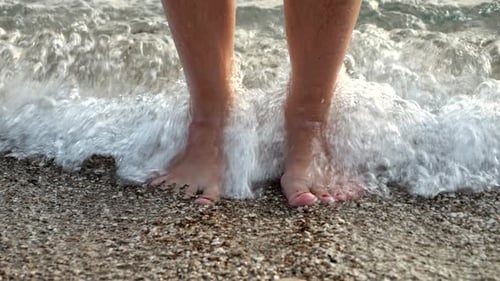 Slow motion of sea waves rolling and breaking on female feet standing on the ocean beach
