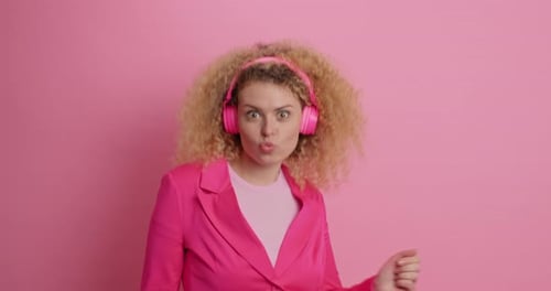 Woman dancing with headphones against pink backdrop