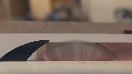A wood board is shaved on a table saw, close up side view in slow motion