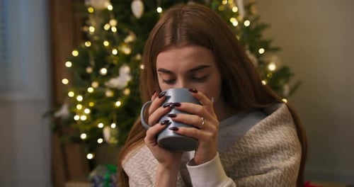 Woman Enjoying Warm Drink by Christmas Tree