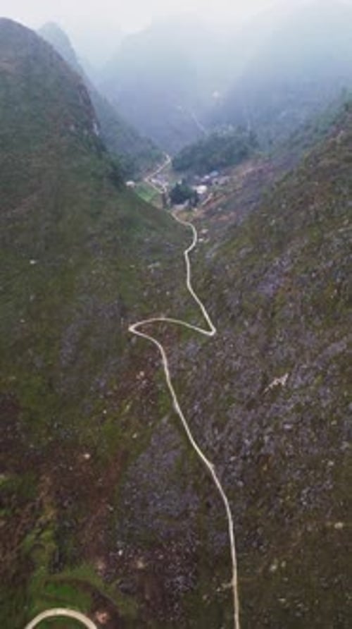 Vue verticale par Drone d'un village de montagne isolé dans une vallée remplie de brouillard avec des collines escarpées