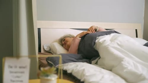 Une grand-mère âgée souffre d'insomnie allongée dans son lit et ne peut pas dormir dans une chambre lumineuse