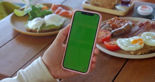 Female Hand Holding Smartphone with Green Screen Chroma Key at Cafe Table with Food Morning
