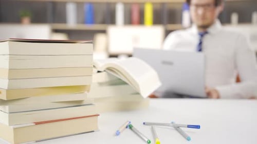 Man working on laptop among pile of books.