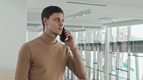 Young Man Talking on Phone in Bright Lobby